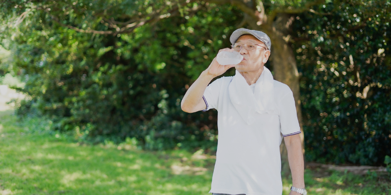 An elderly man wearing white drinking water on a hot day
