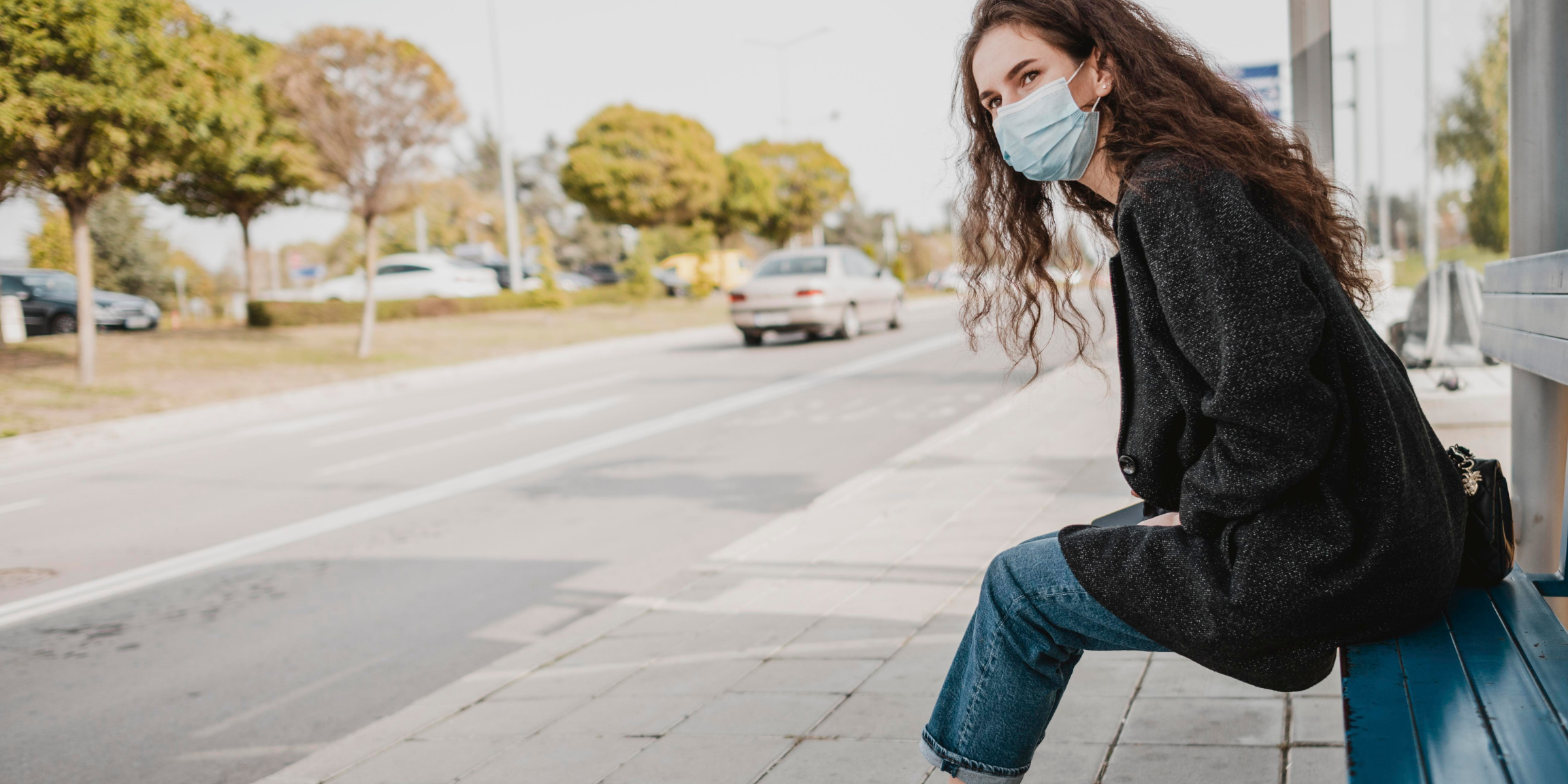 A women wearing a face mask waiting alone at a bus stop