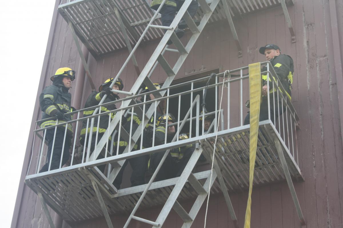 fire fighter recruits in full turnout gear going up a fire escape on a training building