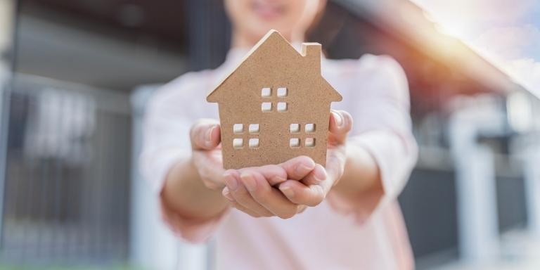 Photo of a person holding a brown figurine of a house in two hands.