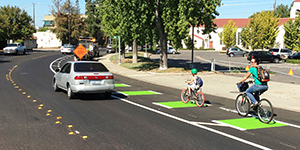 A woman and child riding bikes in a green bike lane next to a car