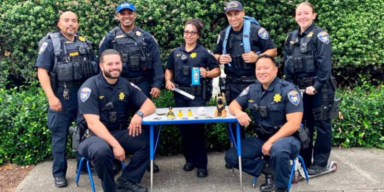Police officers sitting at a childs table wearing backpacks