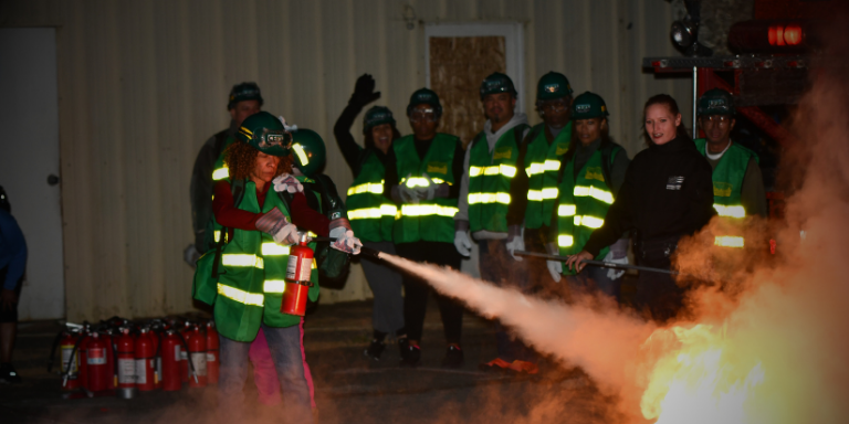 CERT students in green vests practicing putting out fires with fire extinguishers