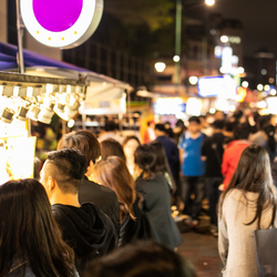 A crowd of people at night in a market with food and wares.