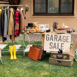 Photo of a garage sale with a rack of coats, table of stuff, and a sign reading garage sale.