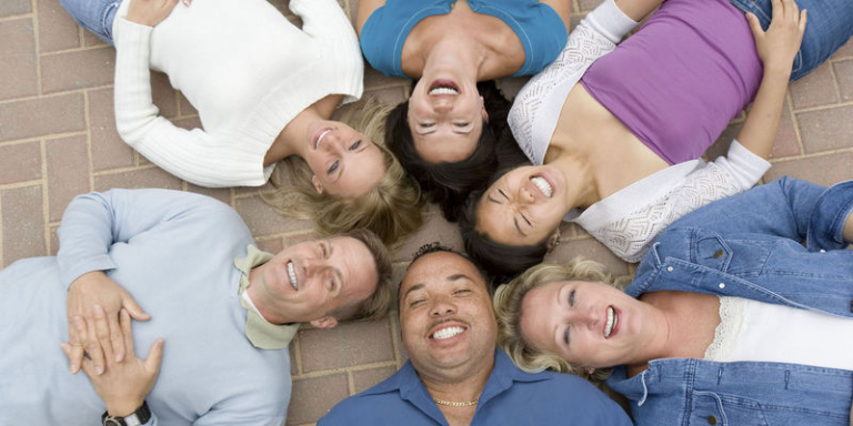 A group of smiling adults lying on the ground in a circle