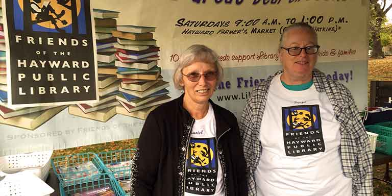Two women standing in front of a Friends of the Hayward Library book sale