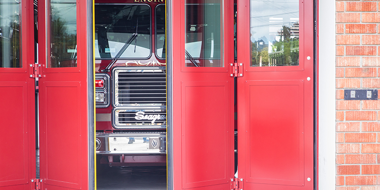 Red fire truck peeking out between a set of red fire doors