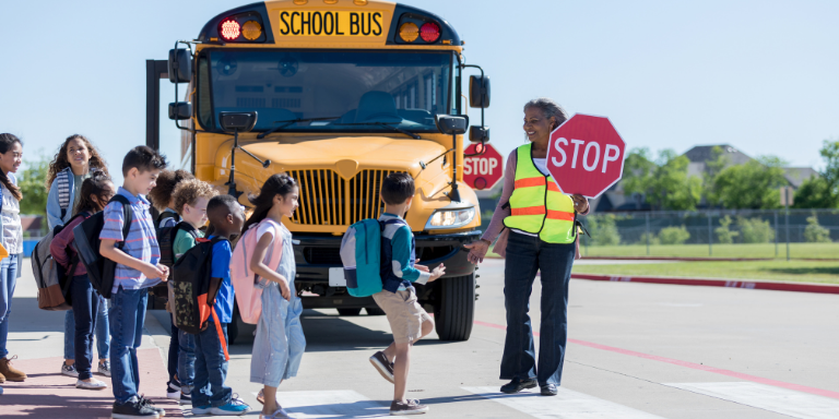 Students crossing the street in front of a school bus with the help of a crossing guard