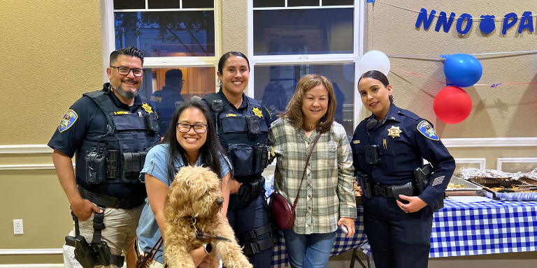 Photo of police officers and community members with a dog posing for a group photo during the 2025 National Night Out event.