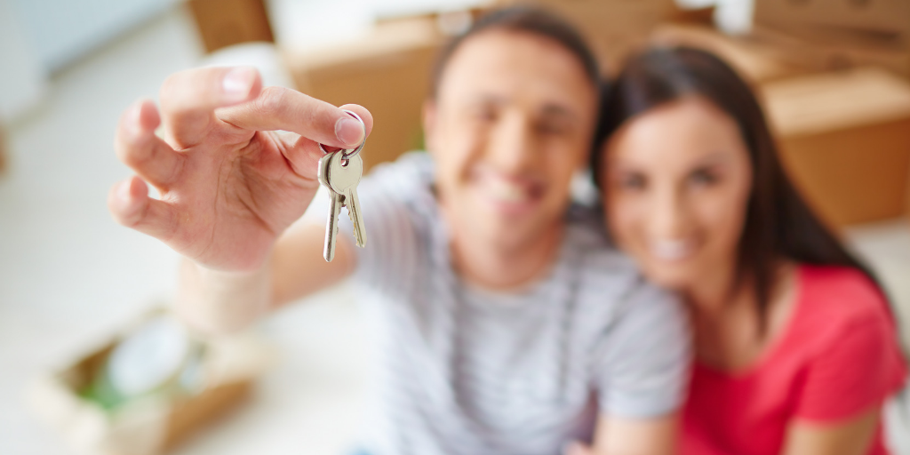 A smiling man holding keys sitting next to a smiling woman