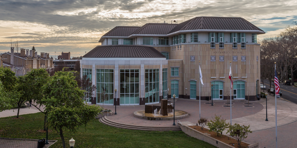 Hayward City Hall on a partly cloudy day. The sky is grey and gold. 