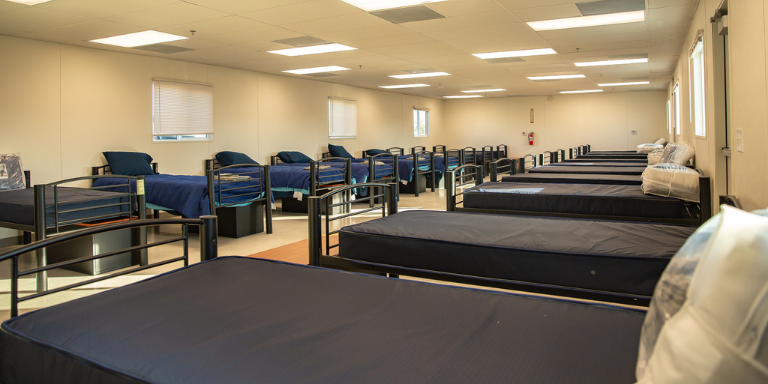 Photo of a long white room lined with navy twin beds and pillows.