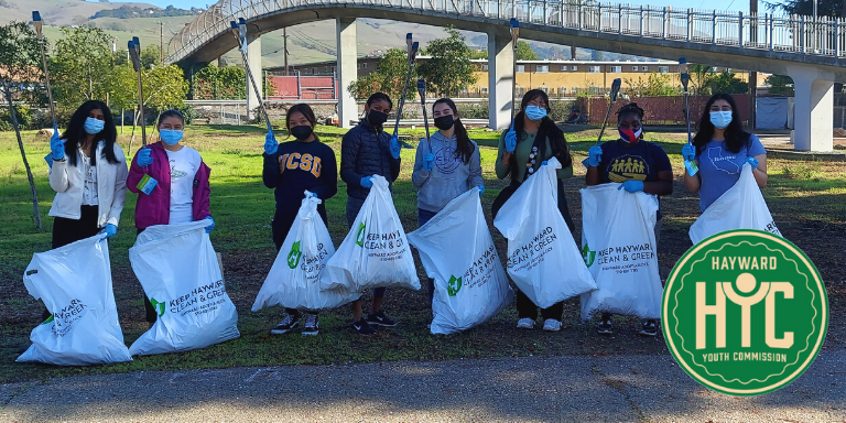 Young students standing in a park holding white trash bags and grabbers