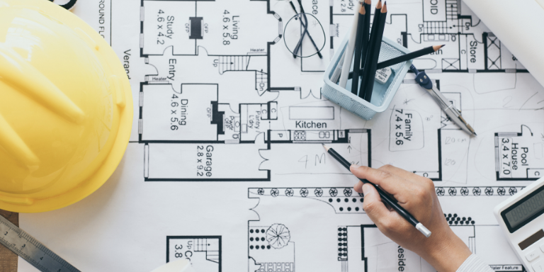 A person working on blue prints next to a yellow hard hat