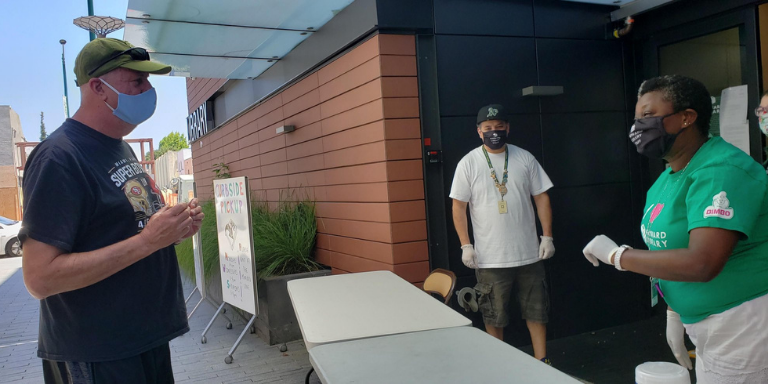 A person wearing a mask talking to two library staff members