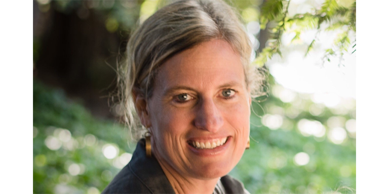 A woman smiling in front of a green gardenscape