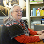 Pam Apostolos sitting at a computer wearing a black sweater and red shirt