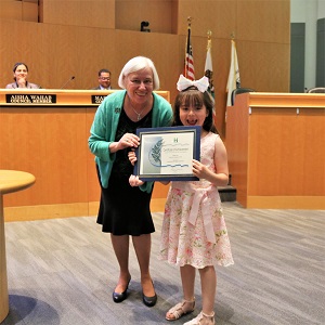 Little girls in a pink and white dress with a big white bow in her hair standing with Mayor Halliday