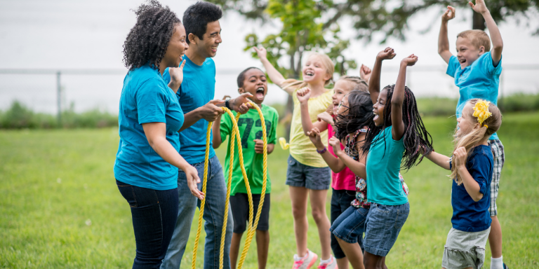 Photo of camp counselors and children playing lawn games, cheering and laughing.