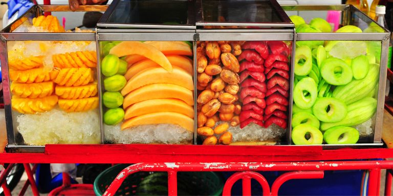 Photo of  a red fruit cart with four glass containers filled with different types of cut up fruit.
