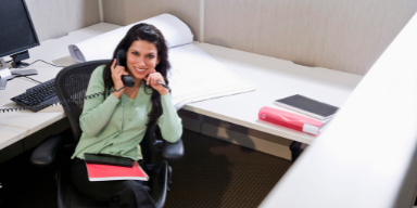 A woman in her cubicle on the phone smiling