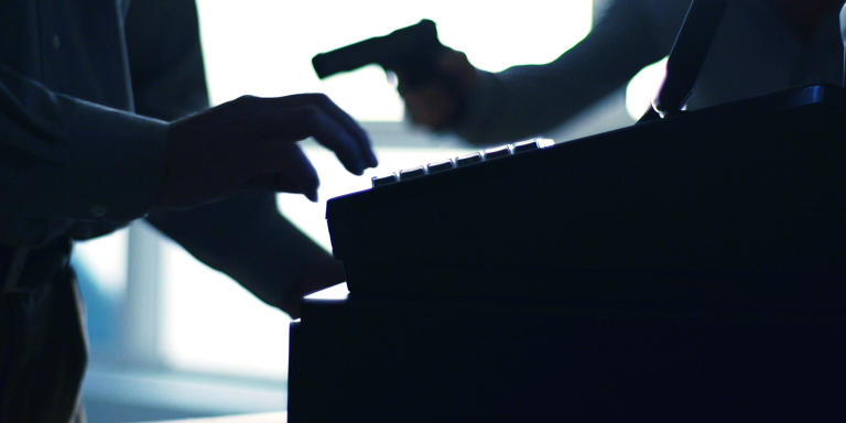 A shadowy figure pointing a fire arm at a cashier