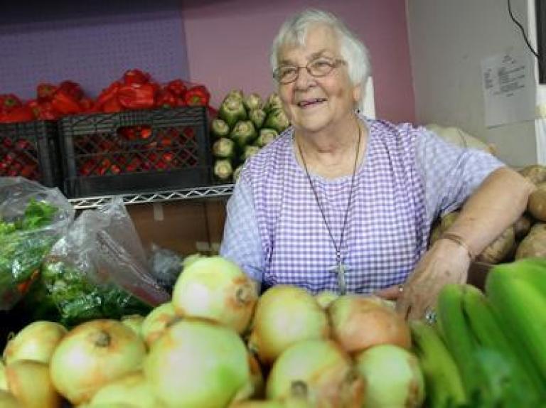 Betty Deforest wearing a purple shirt standing in a room with boxes of fresh food