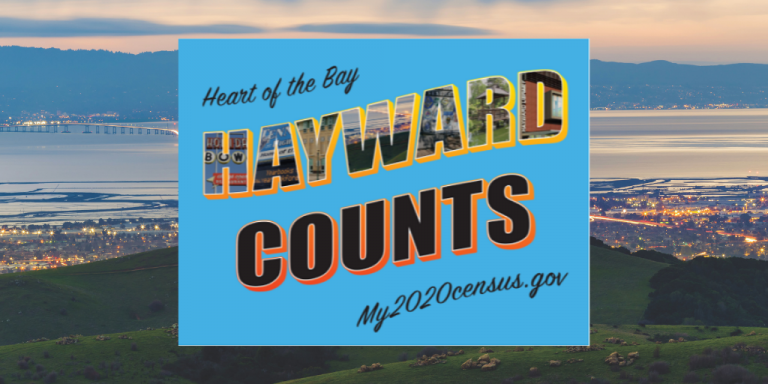 A blue Hayward Counts 2020 Census Sign on top of an image of the Hayward Skyline