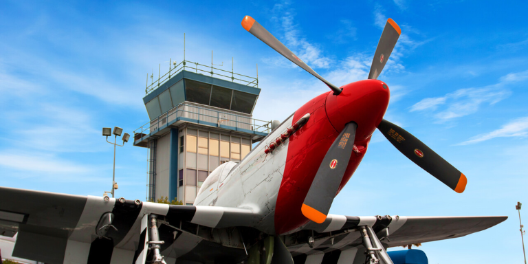 Photo of a propeller airplane in front of a control tower at the Hayward Executive Airport.