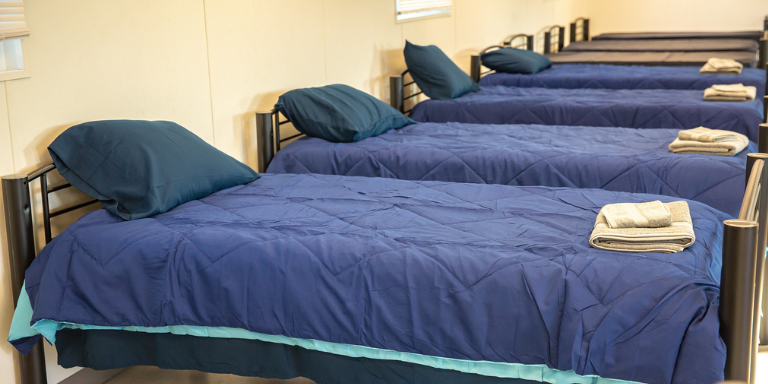Row of beds at the Housing Navigation Center with blue sheets and pillows.