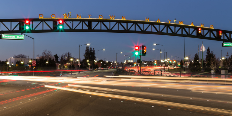 Photo of a busy intersection in Downtown Hayward in the evening with streaks of light. 