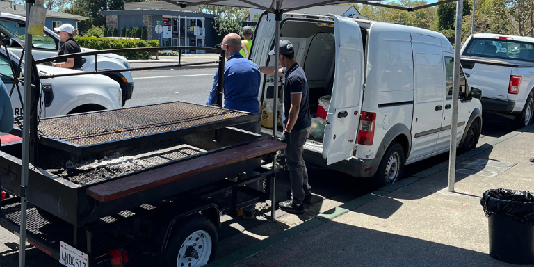 Photo of a barbeque trailer attached to a van. City staff surround the vehicles.